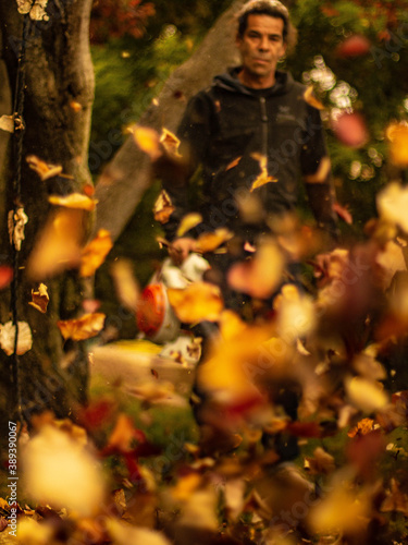 Un homme passe le soufflant dans son jardin , en premier plan on voit les feuilles d'automne qui s'envolent.