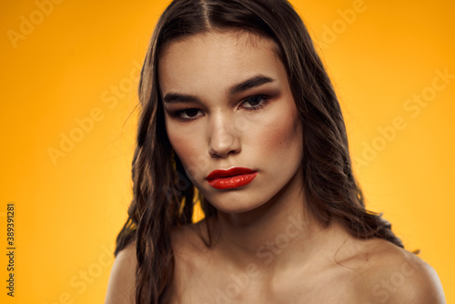 Beautiful brunette naked shoulders bright makeup red lips hairstyle close-up yellow background