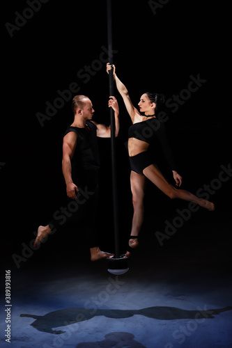 Man and woman doing exercises on pylon isolated on black background.Pole dance concept.