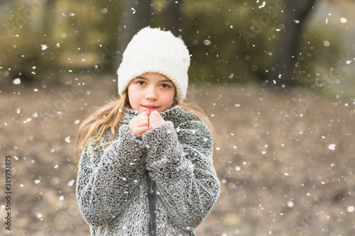 Pretty young girl portrait in winter nature. Girl with white cap and sweatshitr is cold and it is snowing. Winter and cold concept with copy space.