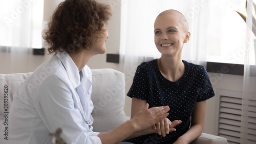 Close up caring doctor holding smiling hairless woman hand, supporting, congratulating with good news, great medical checkup results, remission, young female struggling with cancer, oncology