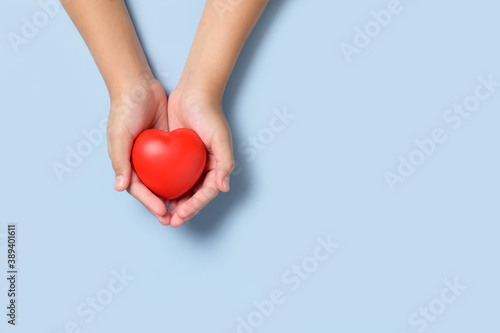 Fototapeta Naklejka Na Ścianę i Meble -  hand child holding red heart on blue background, donation,