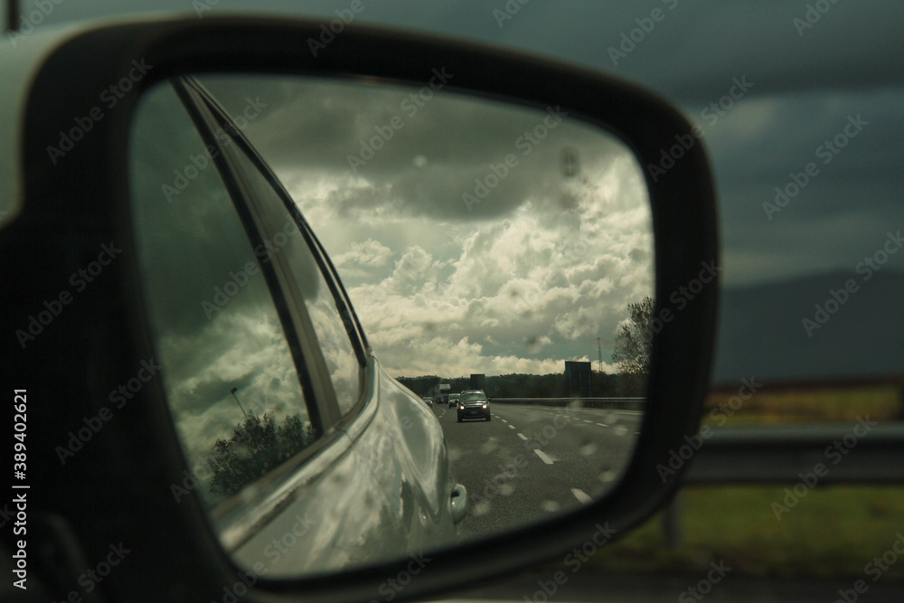 view of the road, reflected from the side mirror of the car, under a blue and cloudy sky