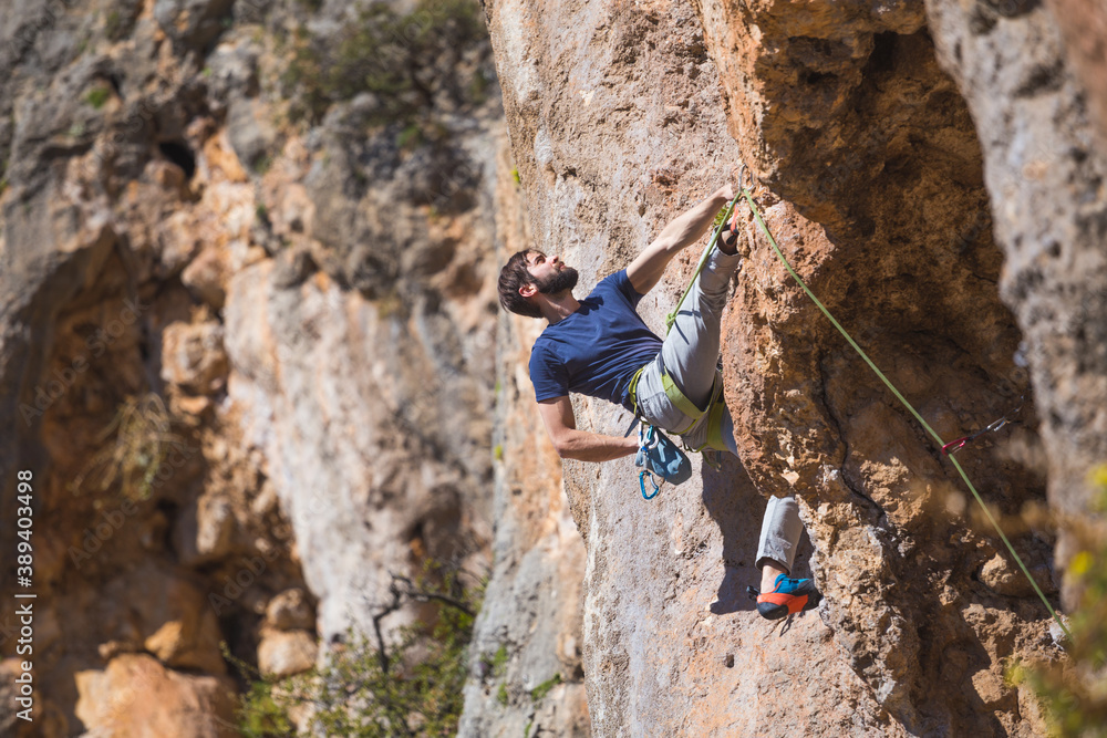 A strong man climbs a beautiful orange rock.