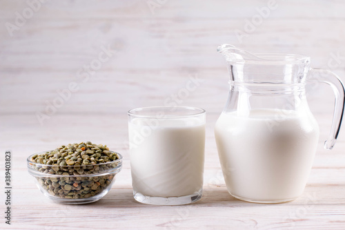 Dry peas, a glass of milk and pea vegetable milk in a milk jug on a white wooden table. Gluten-free, soy free, lactose-free product