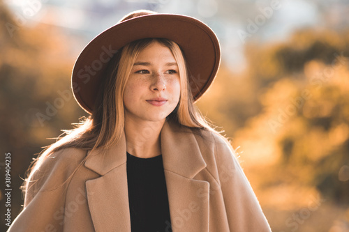Smiling teen girl 12-13 year old wearing stylish hat and beige jacket over yellow nature close up. Teenagerhood. Autumn season. photo