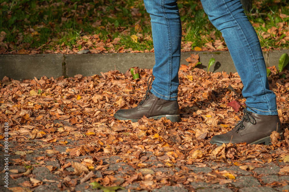 Close up view of woman walking on fallen orange leaves lying on paving stones of avenue in public park. Selective focus. Abstract autumn background. Close up view of woman walking on fallen orange leaves lying on paving stones of avenue in public park. Selective focus. Abstract autumn background.