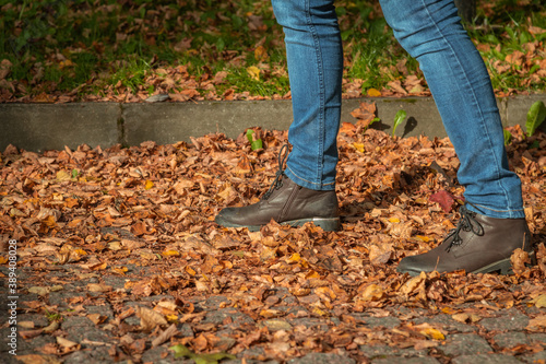 Close up view of woman walking on fallen orange leaves lying on paving stones of avenue in public park. Selective focus. Abstract autumn background.