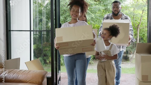 Candid african american family, parents and little girl holding carton box walk into new house move in day,relocate in existing second hand home. Loan mortgage finance in real estate property concept.