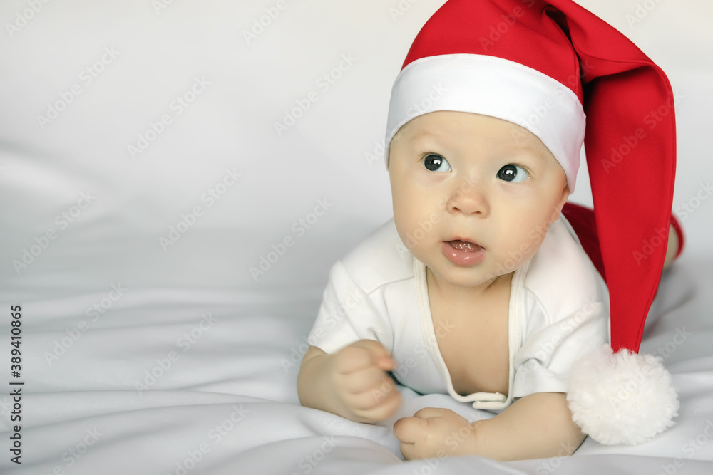 Cute newborn baby in Santa Claus costume with surprised look lies on white sheet Cute newborn baby in Santa Claus costume with surprised look lies on white sheet