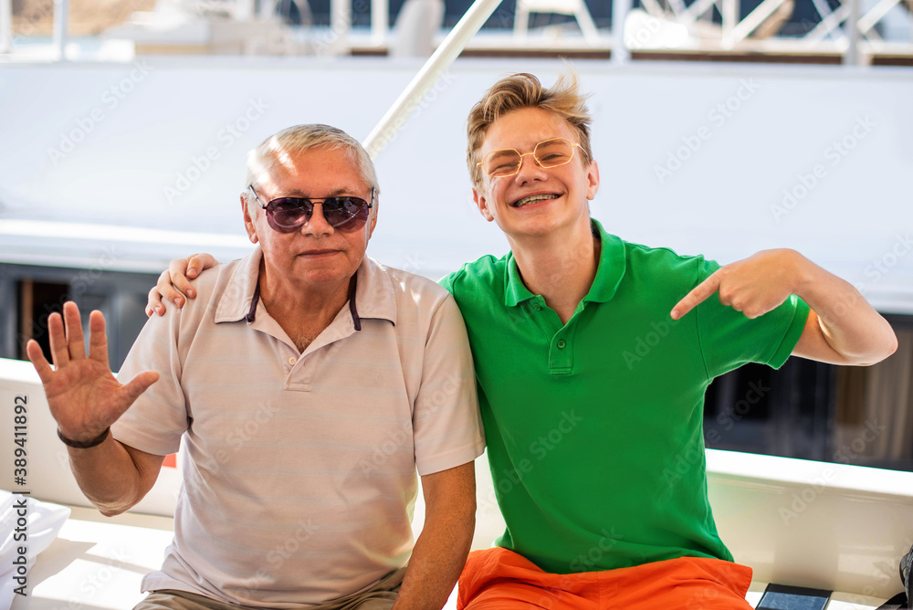 close-up portrait of happy senior man and boy,grandfather and grandson have fun and hugs looking at camera on a background of yachts and a summer sea. close-up portrait of happy senior man and boy,grandfather and grandson have fun and hugs looking at camera on a background of yachts and a summer sea.