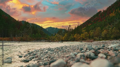 4K UHD Cinemagraph / seamless video loop of a mountain river in the Austrian alps with a vibrant evening sky, close to the German border in autumn. The water is rushing along colorful fall trees.