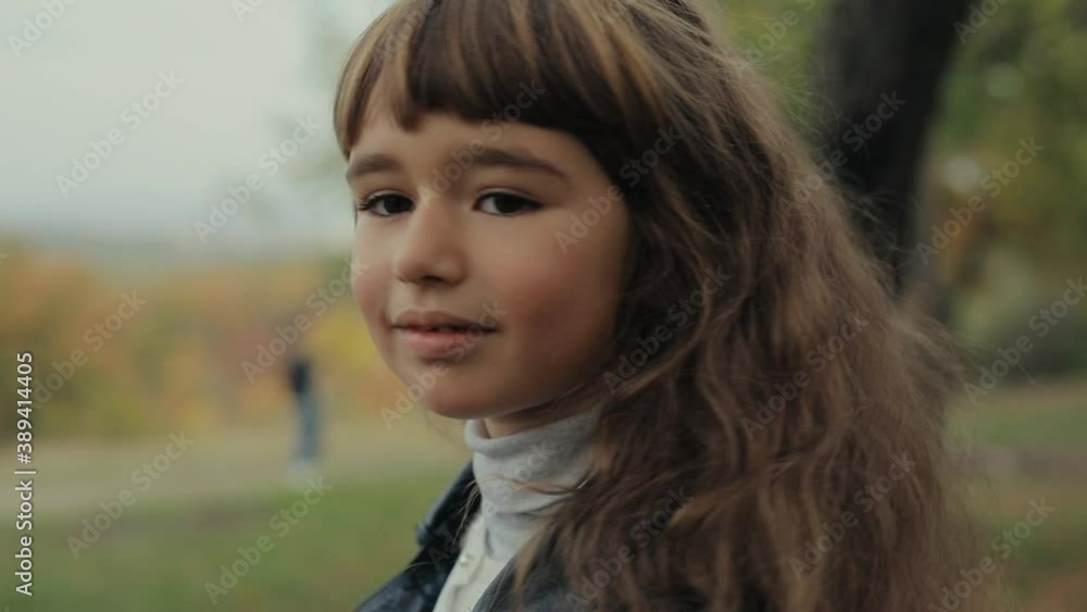 Happy little smiling girl portrait in the autumn forest turning face looks at camera Happy little smiling girl portrait in the autumn forest turning face looks at camera