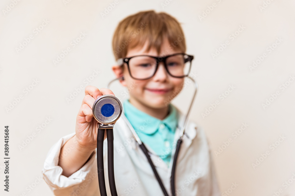 Cute small kid boy wear medical uniform glasses holding stethoscope playing doctor, happy funny little preschool child pretending pediatrician looking at camera, portrait Cute small kid boy wear medical uniform glasses holding stethoscope playing doctor, happy funny little preschool child pretending pediatrician looking at camera, portrait