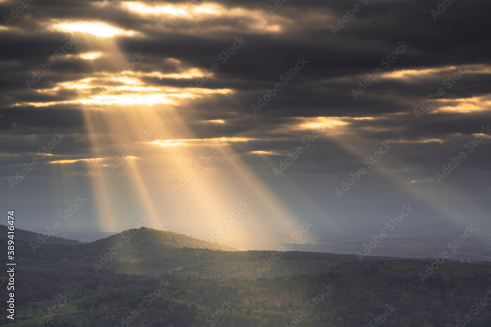 The sun shines through the cloud cover on a mountain range
