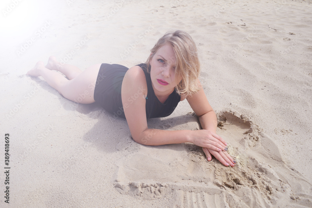 A young woman in a black swimsuit lies on the sand in the desert. The sun shines A young woman in a black swimsuit lies on the sand in the desert. The sun shines