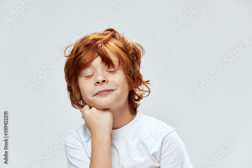 red-haired child with closed eyes holds hand on chin cropped view smile 