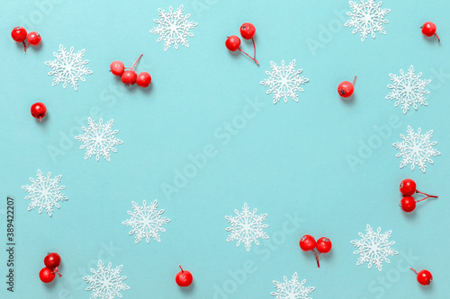 Christmas pattern. White snowflakes, red berry in Christmas composition on pastel blue background for greeting card. Winter festive composition with copy space.