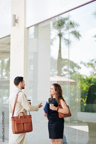 Business people with morning take out coffee standing outdoors and discussing details of work