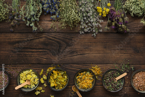 Medicinal plants bunches and row of bowls with dry medicinal herbs on brown wooden board. Top view, flat lay. Alternative medicine. photo