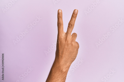 Arm and hand of caucasian young man over pink isolated background counting number 2 showing two fingers  gesturing victory and winner symbol