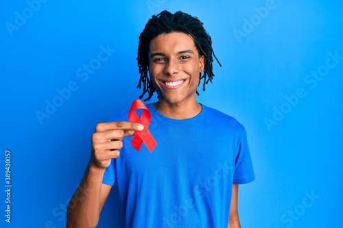 Картината върху платно Young african american man holding support red ribbon looking positive and happy
