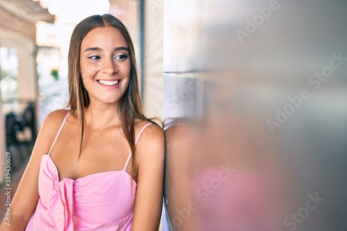 Free Download Young hispanic woman smiling happy leaning on the wall at street of city. - GFXLoad