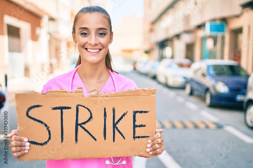 Wallpaper Mural Young hispanic doctor woman smiling happy holding strike banner cardboard at street of city. Torontodigital.ca