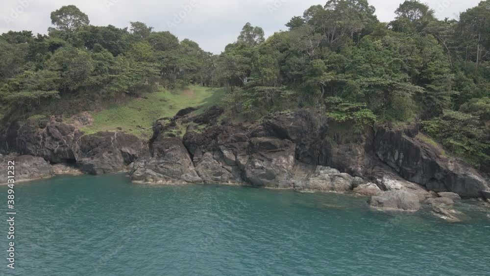Drone left trucking shot , birds eye view of granite rock coastline on a tropical Island with jungle lush green forest and ocean Drone left trucking shot , birds eye view of granite rock coastline on a tropical Island with jungle lush green forest and ocean