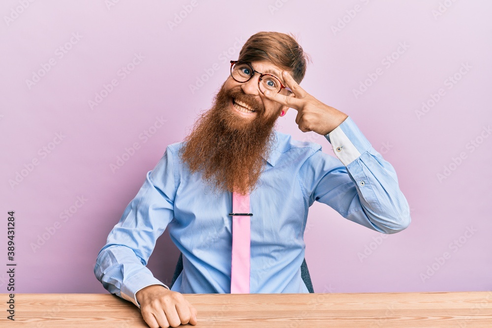 Young irish redhead man wearing business shirt and tie sitting on the table doing peace symbol with fingers over face, smiling cheerful showing victory Young irish redhead man wearing business shirt and tie sitting on the table doing peace symbol with fingers over face, smiling cheerful showing victory