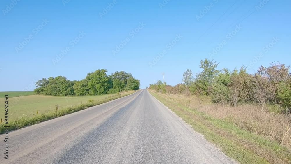 POV while driving on a county paved road in rural Iowa in early autumn; driving past mature fields and standing trees POV while driving on a county paved road in rural Iowa in early autumn; driving past mature fields and standing trees