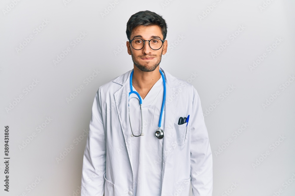 Young handsome man wearing doctor uniform and stethoscope puffing cheeks with funny face. mouth inflated with air, crazy expression.