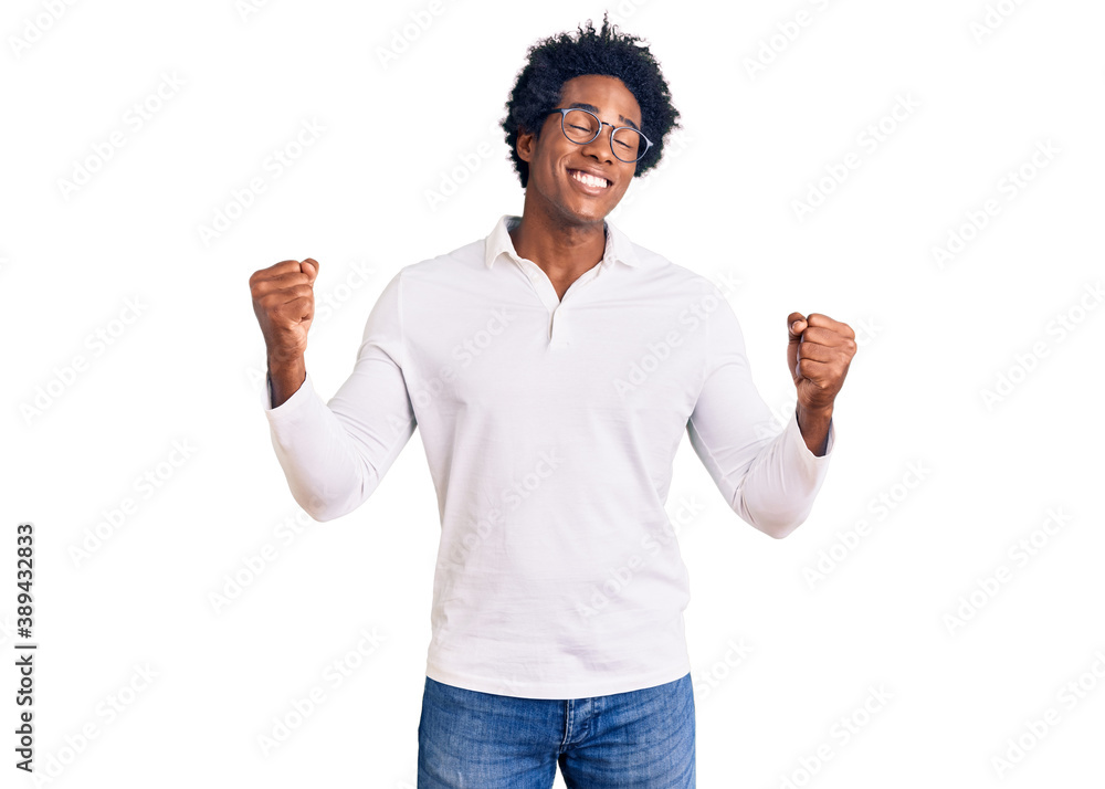Handsome african american man with afro hair wearing casual clothes and glasses very happy and excited doing winner gesture with arms raised, smiling and screaming for success. celebration concept. Handsome african american man with afro hair wearing casual clothes and glasses very happy and excited doing winner gesture with arms raised, smiling and screaming for success. celebration concept.