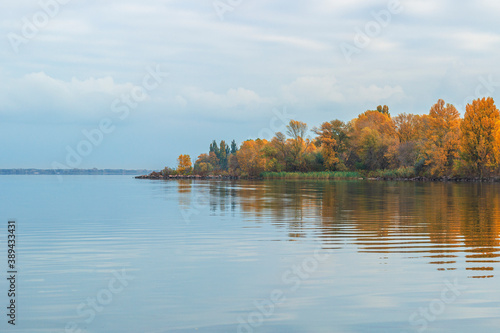 Trees on the shore of a reservoir in autumn, with reflection in the water, autumn landscape