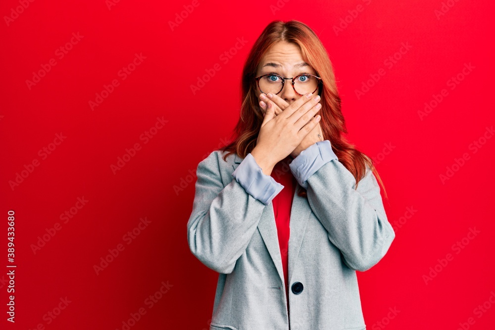 Young redhead woman wearing business jacket and glasses shocked covering mouth with hands for mistake. secret concept. Young redhead woman wearing business jacket and glasses shocked covering mouth with hands for mistake. secret concept.
