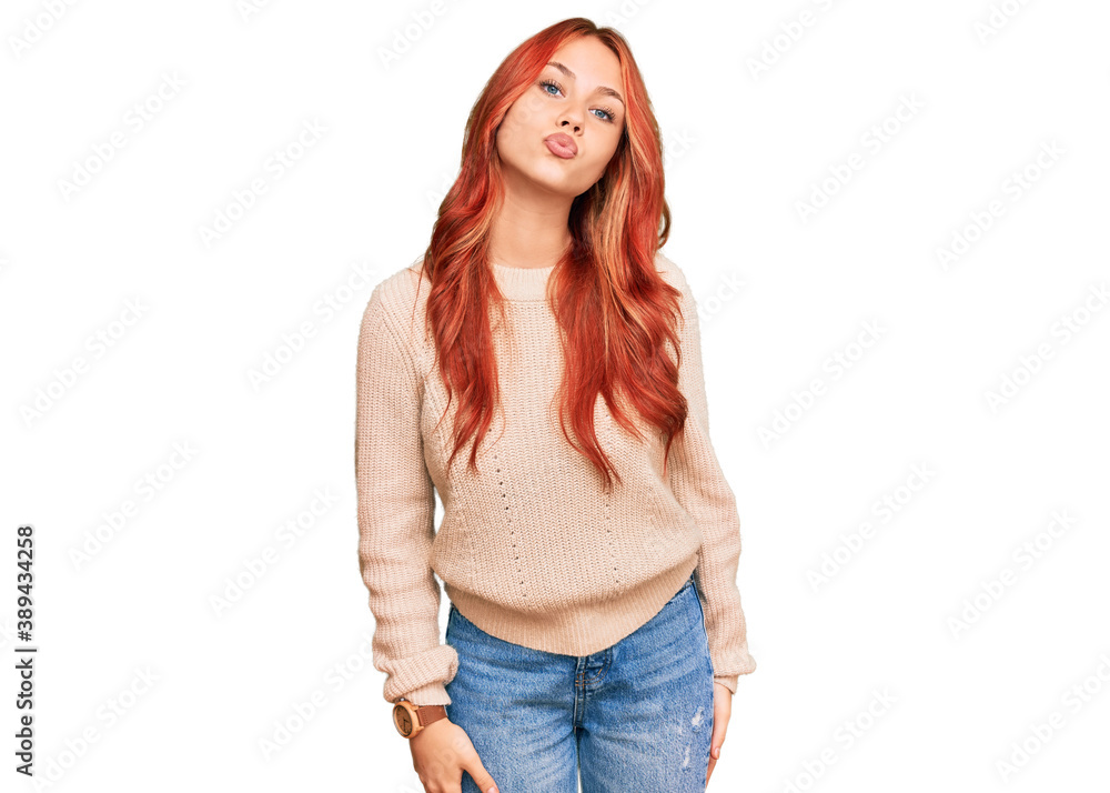 Young redhead woman wearing casual winter sweater looking at the camera blowing a kiss on air being lovely and sexy. love expression.