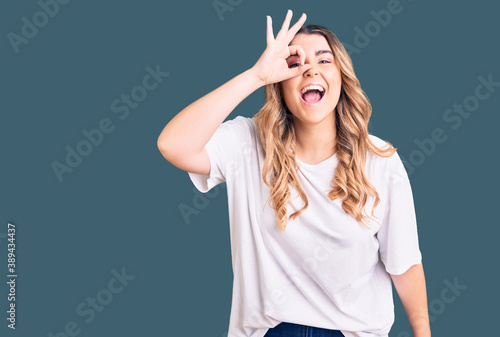 Young caucasian woman wearing casual clothes doing ok gesture with hand smiling, eye looking through fingers with happy face.