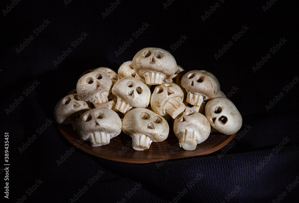 Mushrooms champignons in the form of skulls for Halloween lie in a mountain on a brown plate on a black background Mushrooms champignons in the form of skulls for Halloween lie in a mountain on a brown plate on a black background