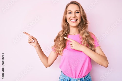 Young caucasian woman with blond hair pointing with fingers to the side smiling with a happy and cool smile on face. showing teeth.