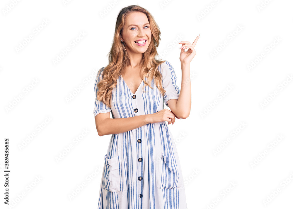 Young caucasian woman with blond hair wearing summer dress smiling happy pointing with hand and finger to the side Young caucasian woman with blond hair wearing summer dress smiling happy pointing with hand and finger to the side