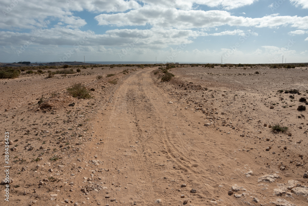 Dirt road with Atlantic Ocean in the background. Barlovento desert area, Fuerteventura, Canary Islands. Dirt road with Atlantic Ocean in the background. Barlovento desert area, Fuerteventura, Canary Islands.