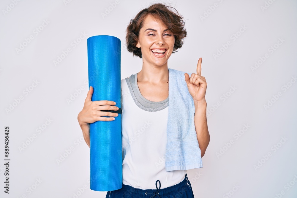 Young hispanic woman holding yoga mat smiling with an idea or question pointing finger with happy face, number one Young hispanic woman holding yoga mat smiling with an idea or question pointing finger with happy face, number one