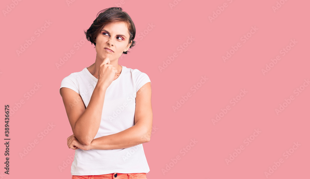 Beautiful young woman with short hair wearing casual clothes serious face thinking about question with hand on chin, thoughtful about confusing idea Beautiful young woman with short hair wearing casual clothes serious face thinking about question with hand on chin, thoughtful about confusing idea