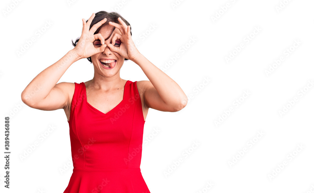 Beautiful young woman with short hair wearing casual style with sleeveless shirt doing ok gesture like binoculars sticking tongue out, eyes looking through fingers. crazy expression. Beautiful young woman with short hair wearing casual style with sleeveless shirt doing ok gesture like binoculars sticking tongue out, eyes looking through fingers. crazy expression.