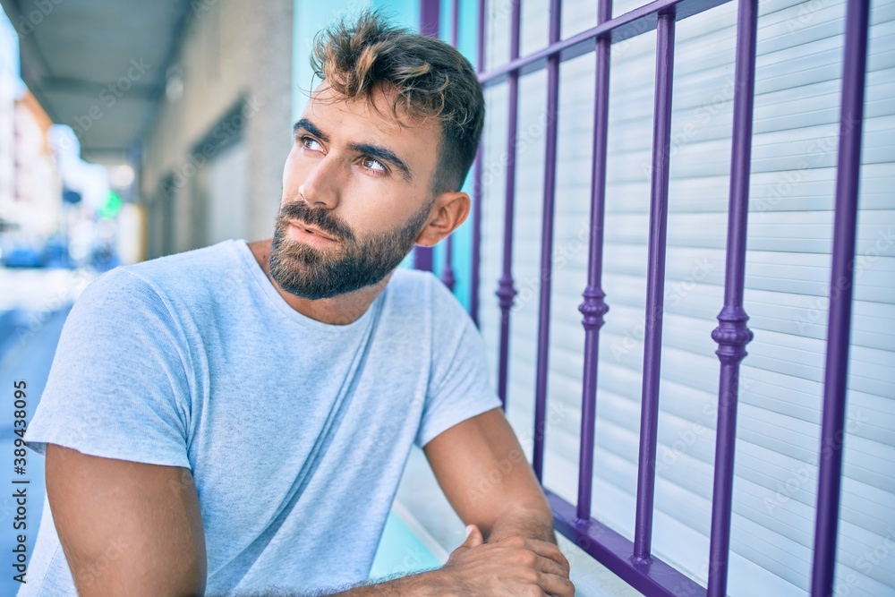 Young hispanic man with serious expression leaning on the wall at the city