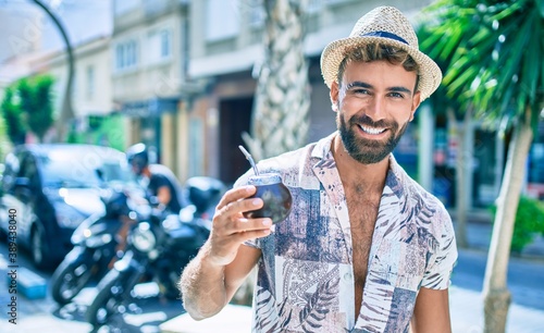 Young hispanic man on vacation smiling happy drinking mate tea at street of city photo