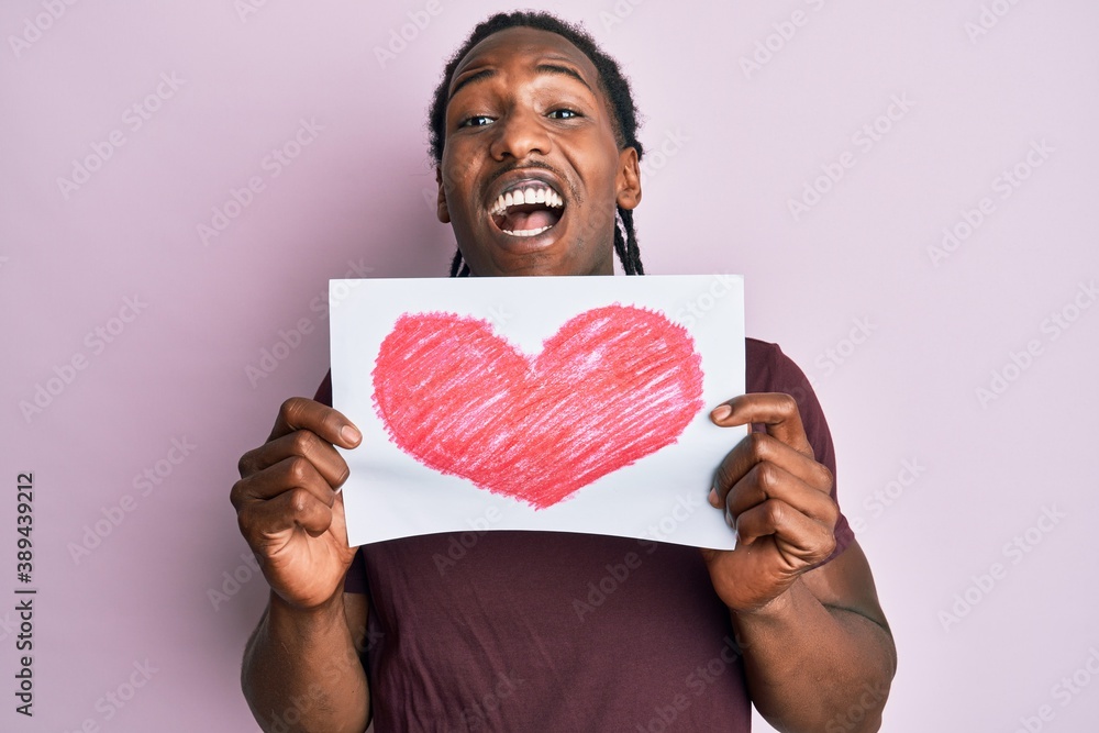 African american man with braids holding heart draw celebrating crazy and amazed for success with open eyes screaming excited. African american man with braids holding heart draw celebrating crazy and amazed for success with open eyes screaming excited.