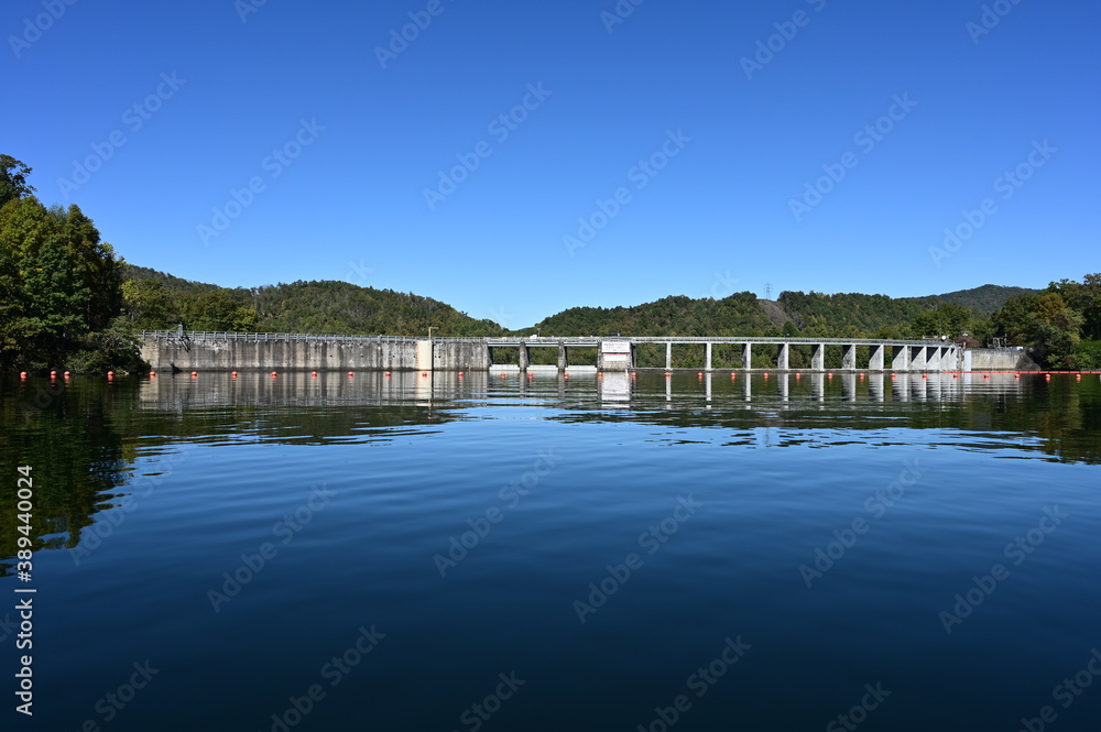 Fototapeta premium Santeetlah Dam on Lake Santeetlah and Cheoah River in Graham County, North Carolina reflected in calm water of lake on clear autumn afternoon.