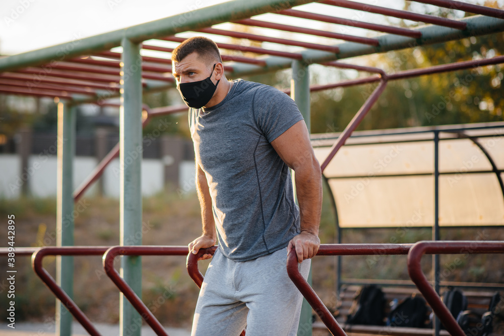 A young man does push-UPS, pull-UPS on a sports field in a mask during a pandemic at sunset. Sports, healthy lifestyle