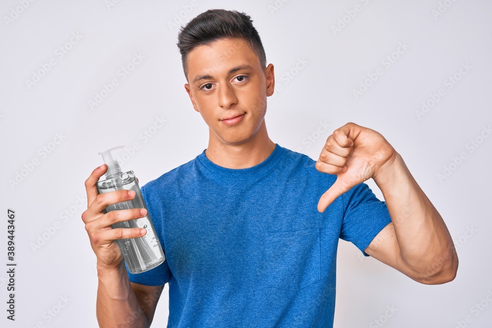 Young hispanic boy using hand sanitizer gel with angry face, negative sign showing dislike with thumbs down, rejection concept Young hispanic boy using hand sanitizer gel with angry face, negative sign showing dislike with thumbs down, rejection concept